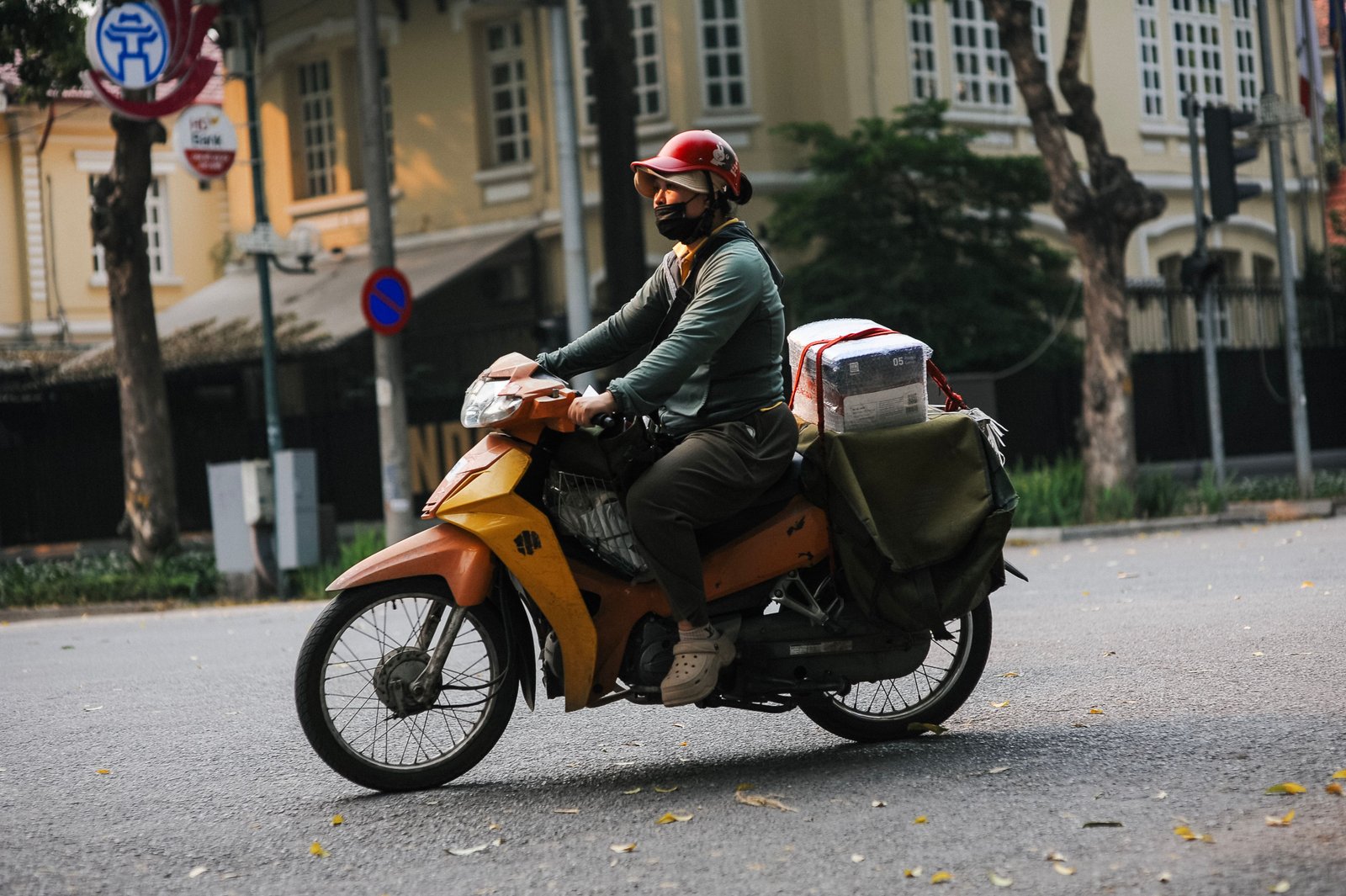 Motoboy de uniforme entregando pacote em via urbana, ao lado de uma loja com placa de horário de funcionamento em feriado