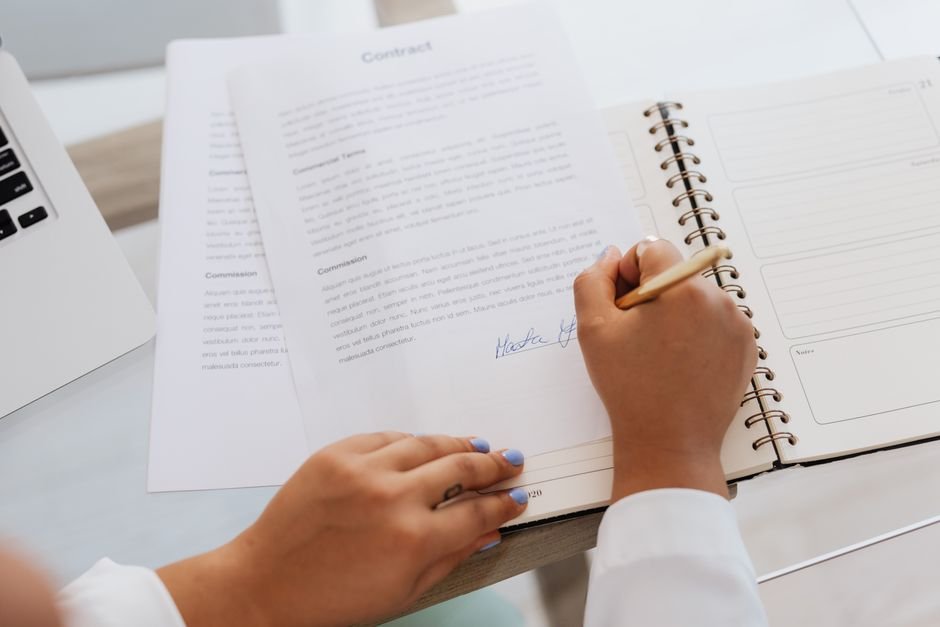 Dona de lavanderia analisando contratos de prestação de serviço com funcionária que opera máquina de passar roupa